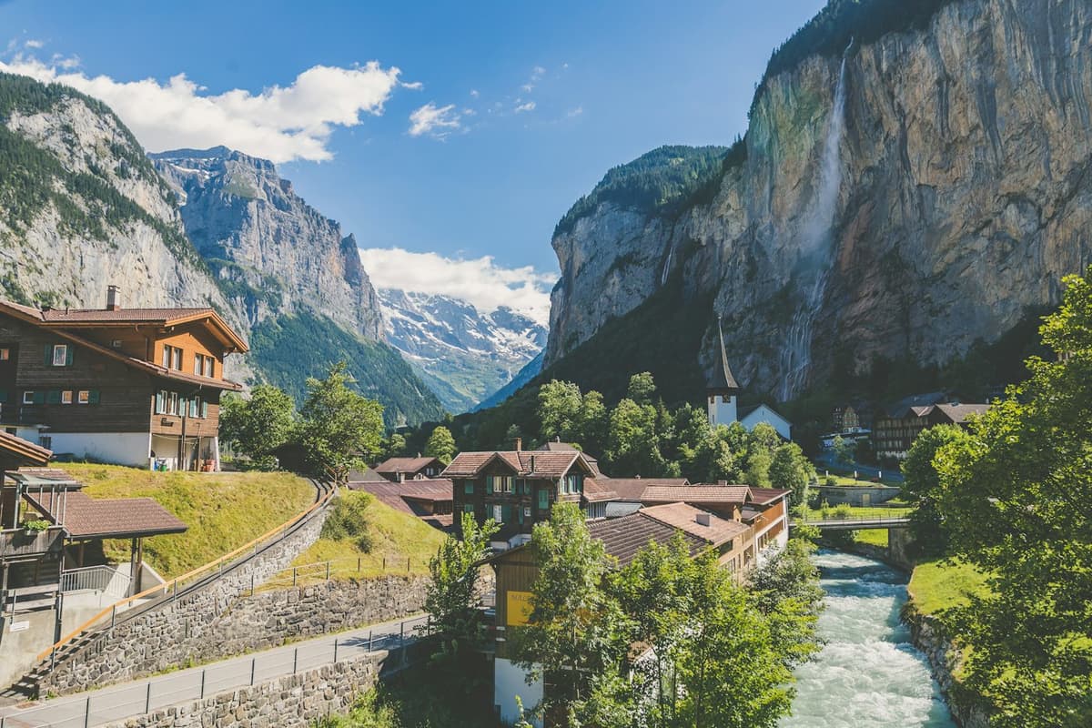 Alpendorf in einem grünen Tal unter Wasserfällen und Felswänden